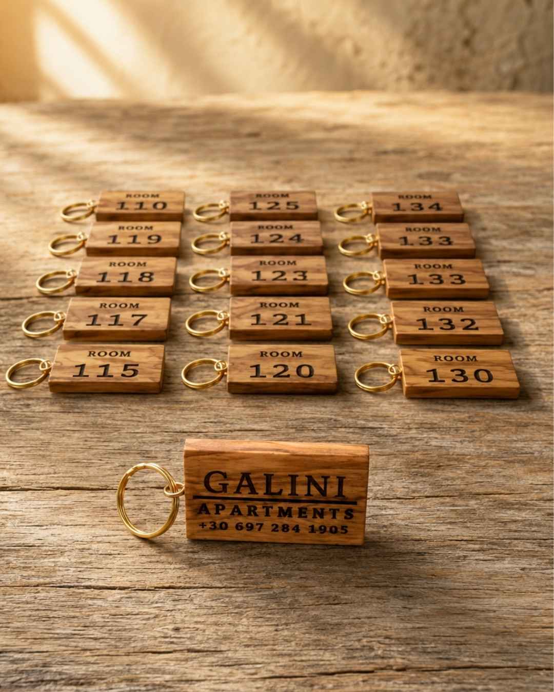Olive wood room-number keychains laser-engraved for Galini Apartments, arranged in a grid on a rustic wooden surface