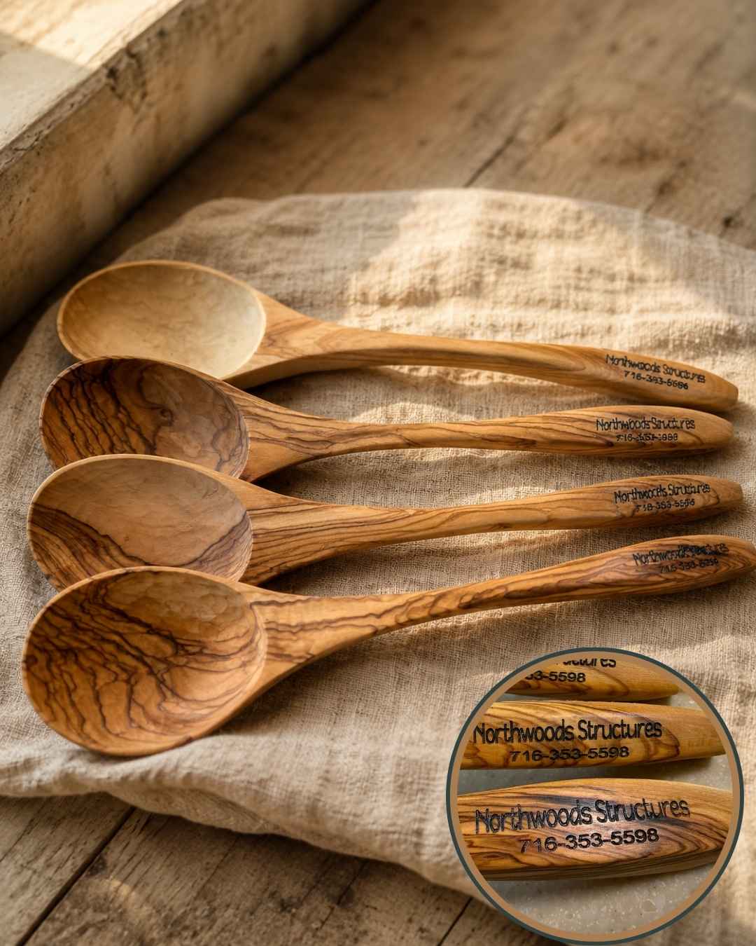 Four olive wood spoons laser-engraved with the Northwoods Structures business name and phone number, arranged on linen