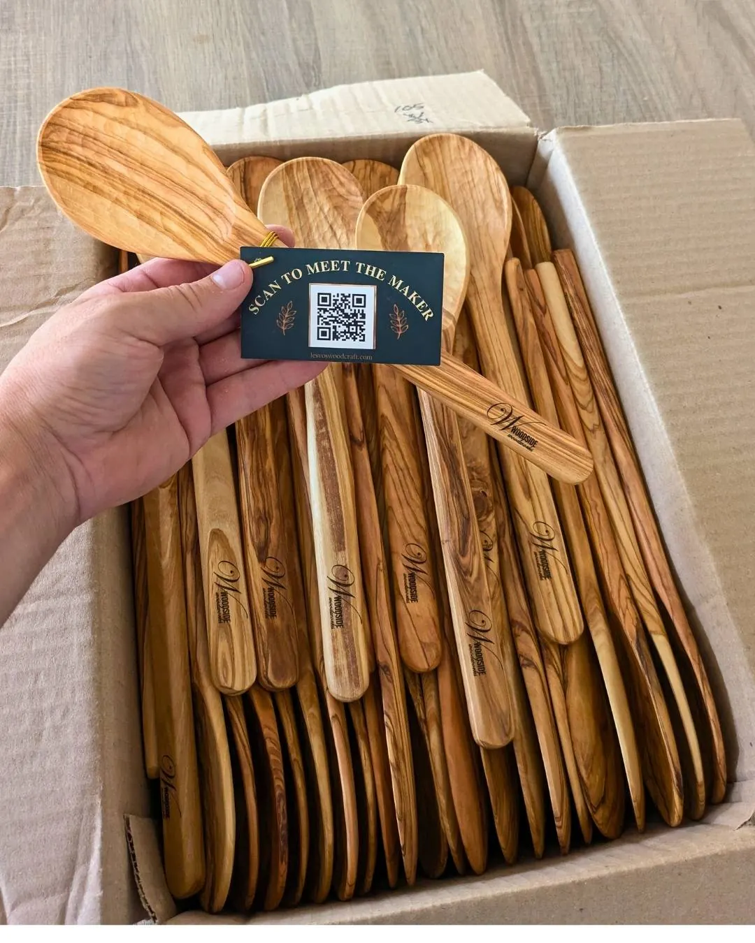 Box of olive wood spoons laser-engraved with the Woodside Woodworks logo, held with a scan-to-meet-the-maker tag