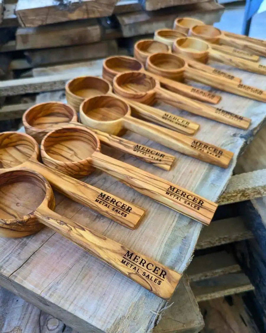 Rows of olive wood coffee scoops laser-engraved for Mercer Metal Sales in the workshop
