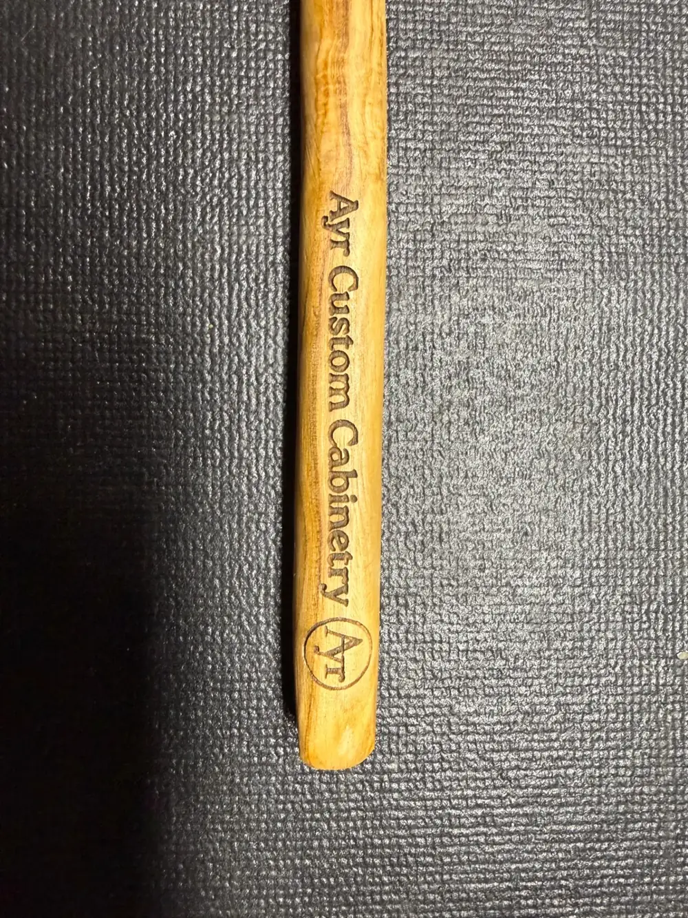 Olive wood spoon handle laser-engraved with the Ayr Custom Cabinetry business name and logo
