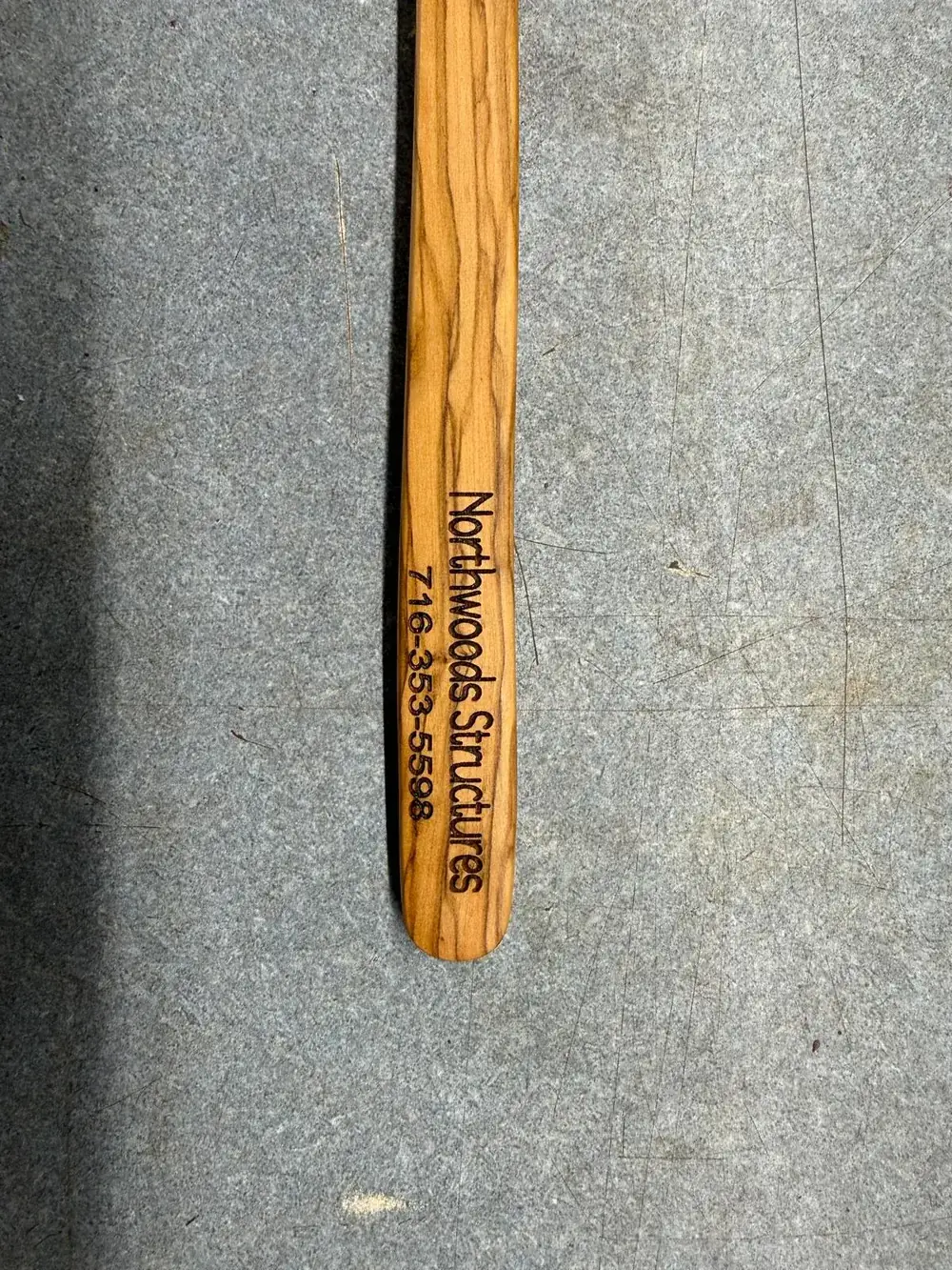 Olive wood utensil engraved with Northwoods Structures business name and phone number
