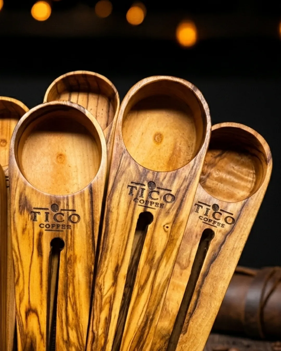 Olive wood coffee scoops engraved with the Tico Coffee logo, displayed against a dark background