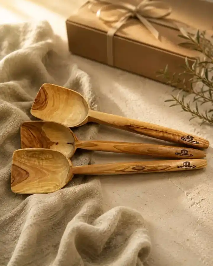 Three olive wood spoons laser-engraved with the Lesvos Woodcraft logo, arranged on linen next to a kraft gift box tied with ribbon